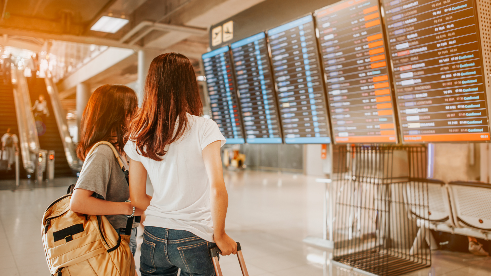 Two people looking at airport departures and arrivals signage.