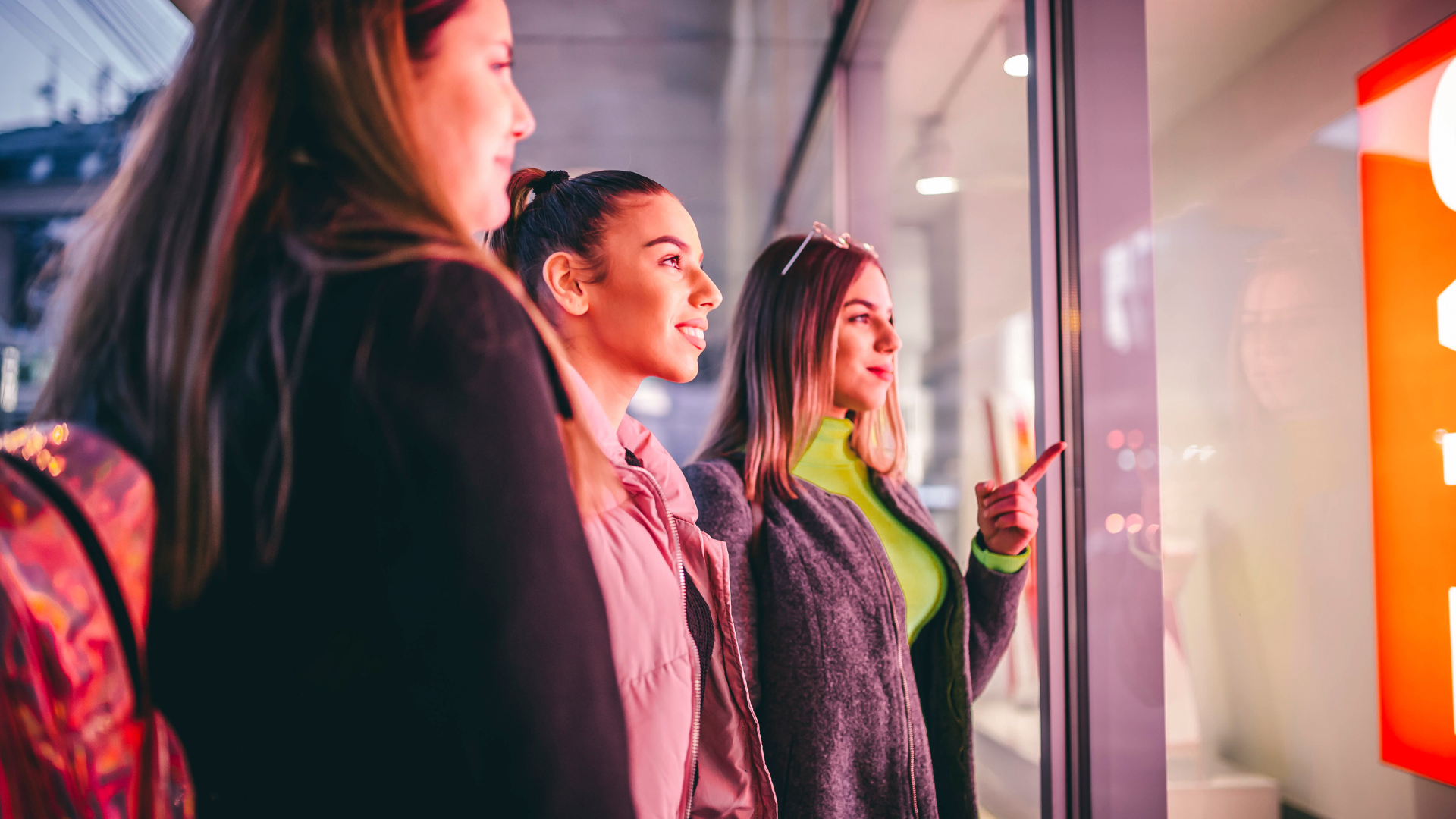 Three young women looking into retail window at digital signage