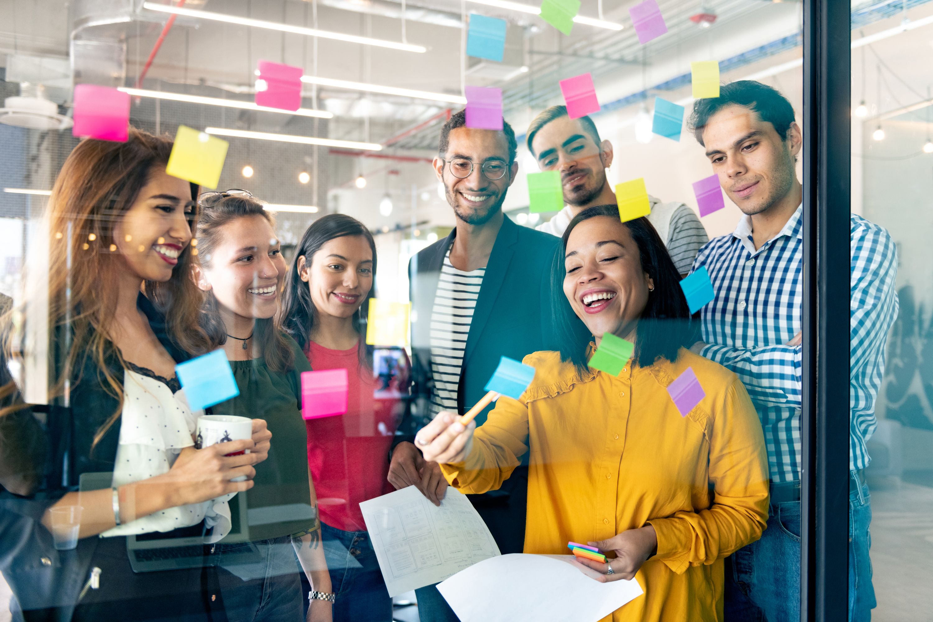 Office workers adding sticky notes to a wall with ideas during a brainstorming session.