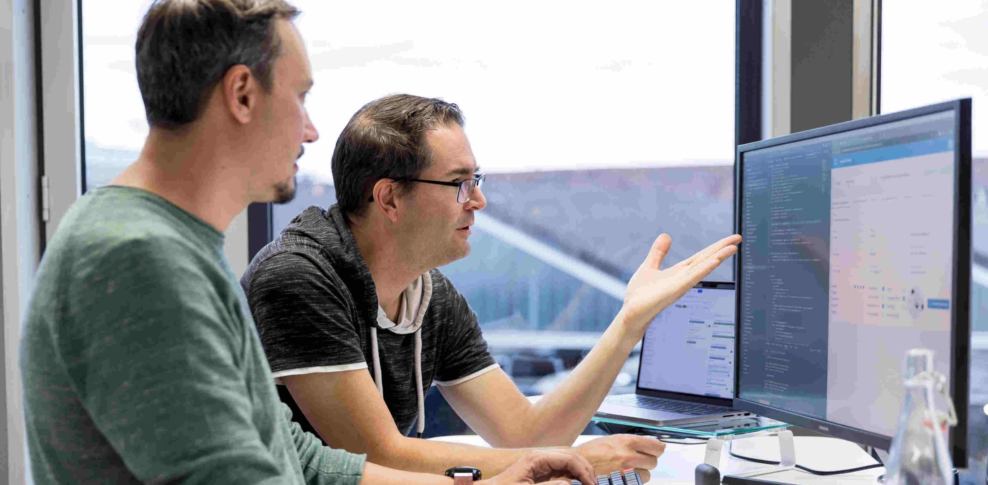 Zwei Software Entwickler diskutieren über Code an einem Bildschirm