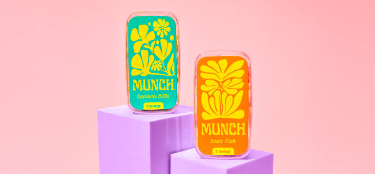 Bright, colorful product packaging with bold illustrated labels on small containers displayed on pastel blocks against a pink background