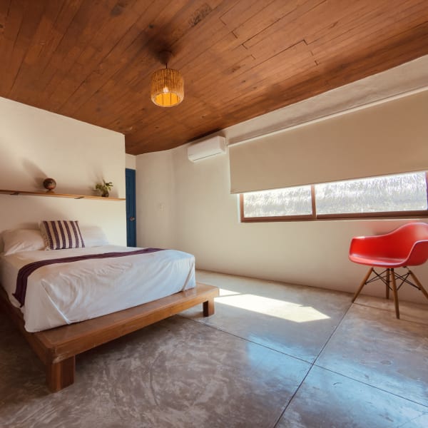 Habitación Jamaica con cama matrimonial de madera, techo de madera y silla roja junto a la ventana