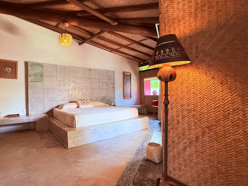 Habitación Petate con cama sobre base de concreto, muros de petate y lámpara de pie