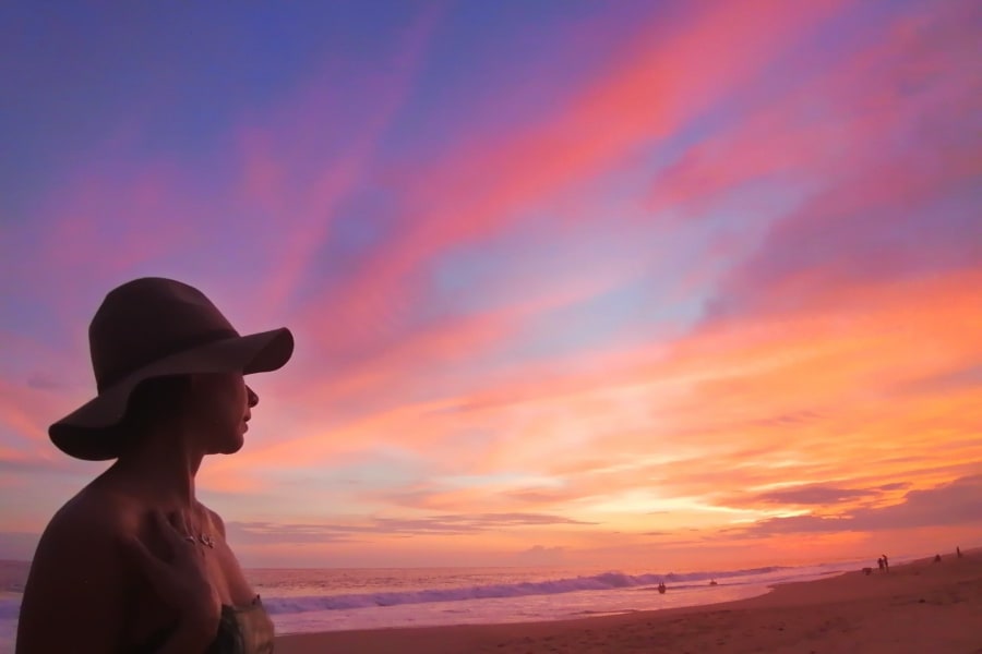 Mujer con sombrero frente al atardecer en la playa