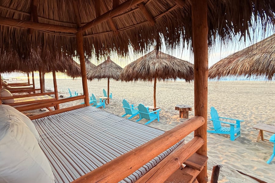 Camas balinesas bajo palapa y sillas azules en la playa