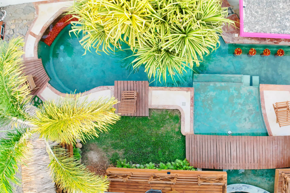 Vista aérea de la alberca turquesa, el jardín y las palmeras del club