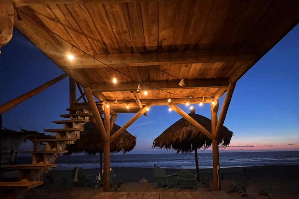 Palapa de madera con luces frente al mar al anochecer