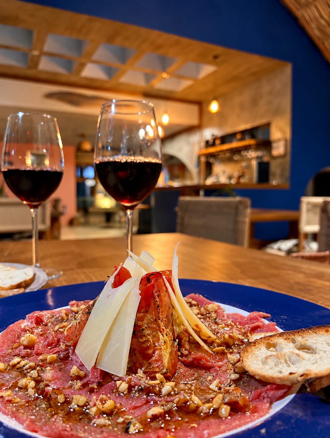 Carpaccio con láminas de queso y pan, con dos copas de vino tinto