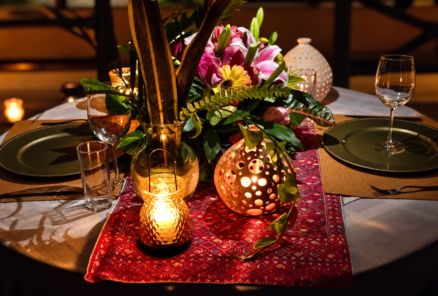 Mesa con flores, velas y una lámpara de barro calado sobre un camino de mesa rojo