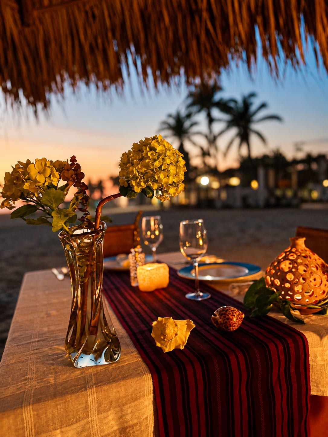 Mesa para dos con flores y velas bajo la palapa, con palmeras al atardecer