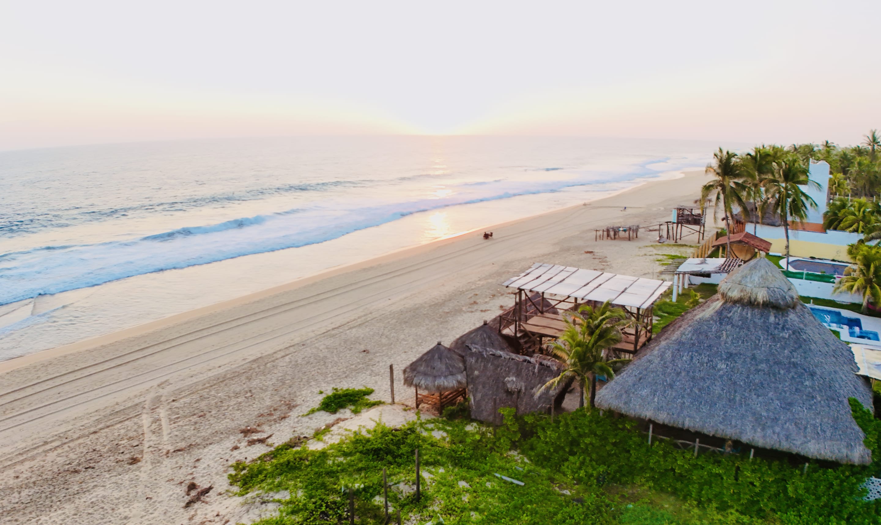 Vista aérea del club de playa con palapas frente al mar al atardecer