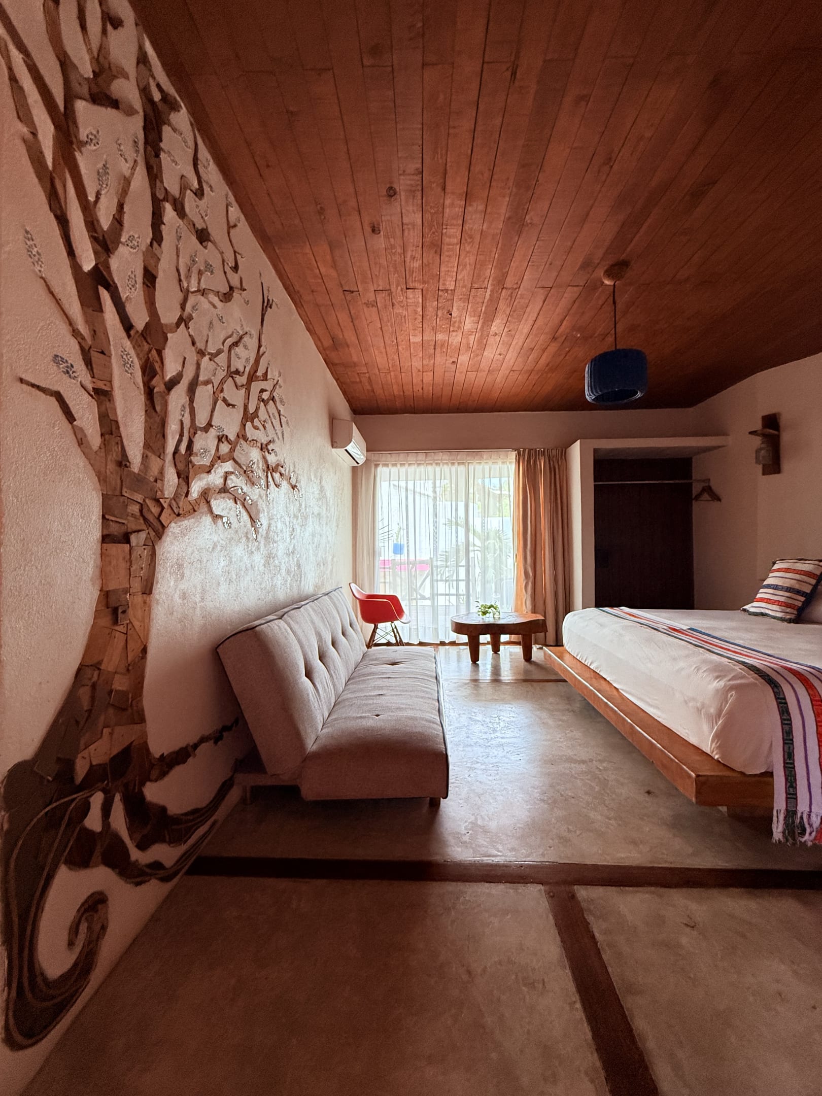 Habitación con un mural de árbol en la pared, sofá y cama junto al ventanal