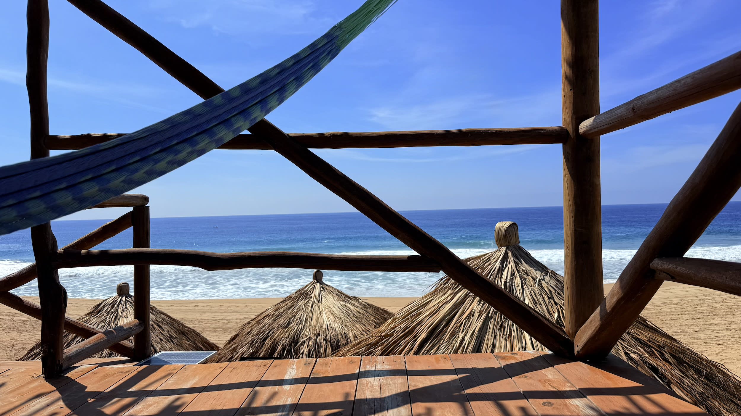 Vista desde la hamaca de un mirador de madera hacia las palapas del club de playa y el mar