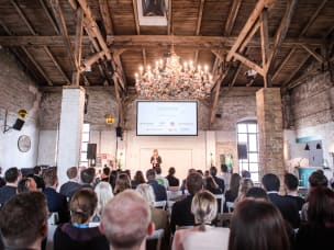 Event Saal mit Bühne, Franziska Kolbe hält Vortrag vor vielen Teilnehmern 