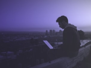 Mann sitzt mit Laptop auf einer Mauer