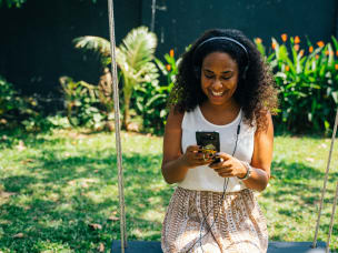 Person smiling at phone, sitting in between green plants, amid Beagle Button's new eco shopping extension
