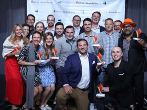 A group of seventeen people, seven of them holding awarded prizes, at the ThinkTank Network Awards.
