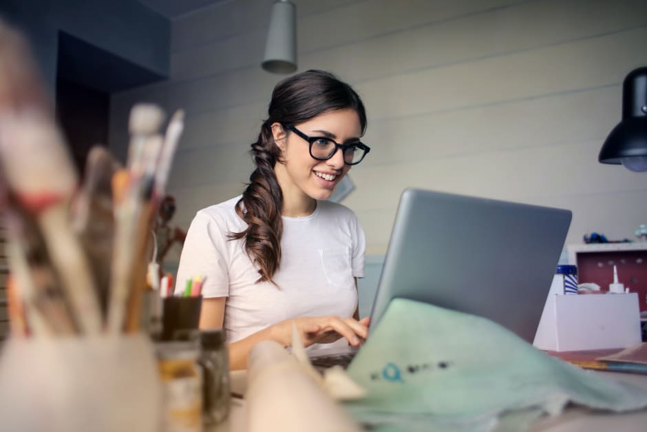 Frau mit Brille sitzt am Laptop und lächelt