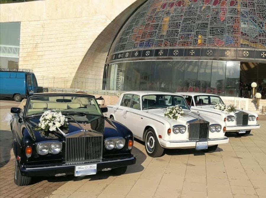 White Rolls-Royce Silver Shadows and a dark blue Corniche decorated with flowers outside a church