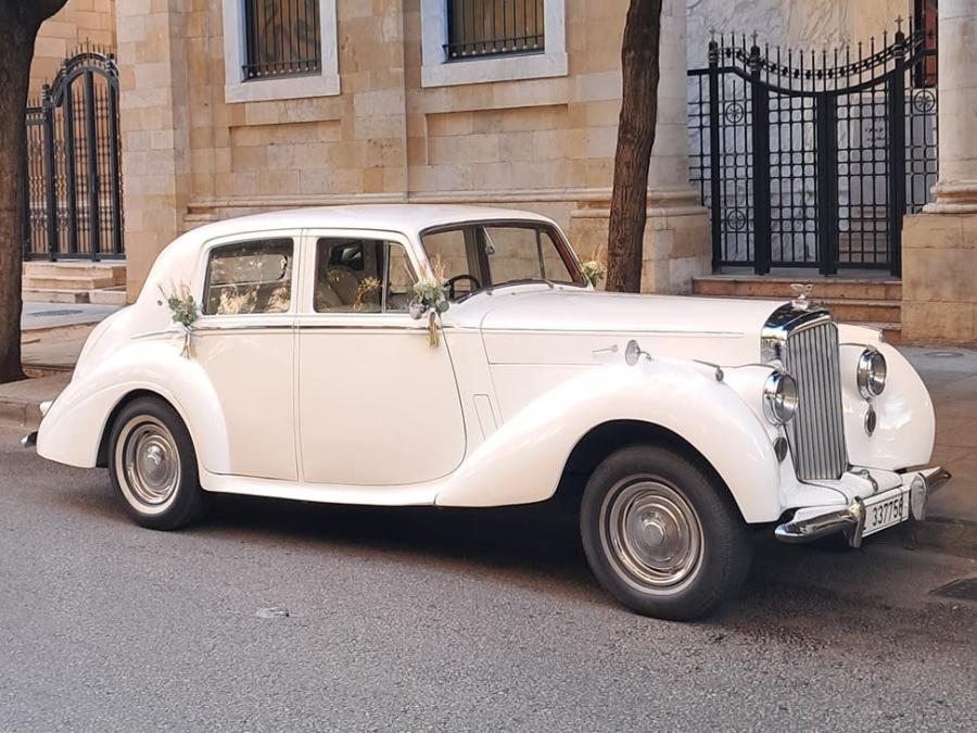 Side view of the white 1953 Bentley R Type in front of a stone house