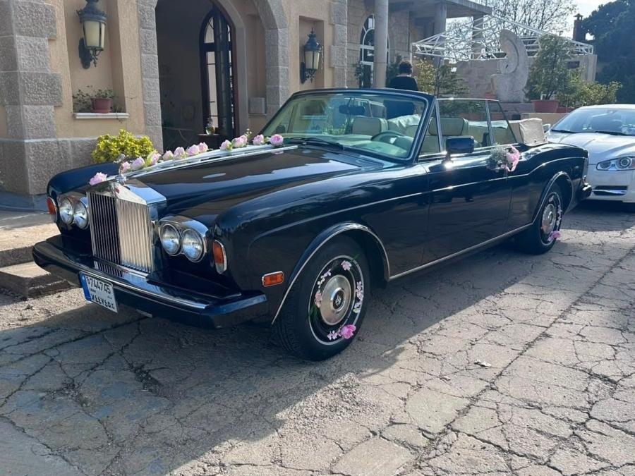 Dark blue Rolls-Royce Corniche convertible with flower garlands, by an old stone house