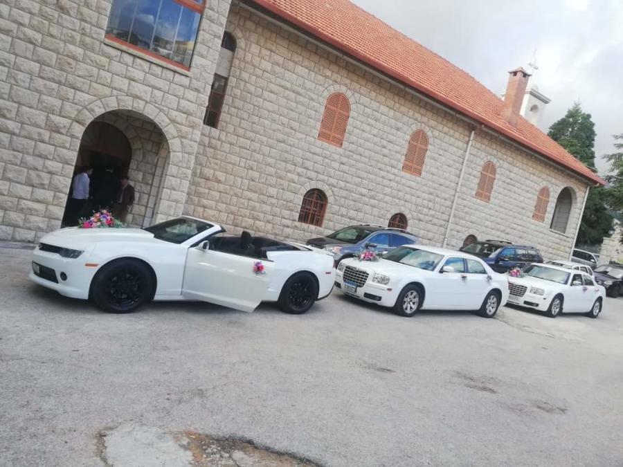 White Camaro convertible and two white Chrysler 300C sedans outside an old stone church
