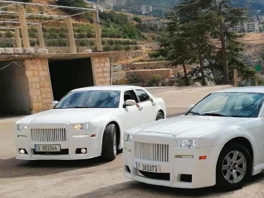 Two white Chrysler 300C Phantom-look sedans parked together by a stone arch