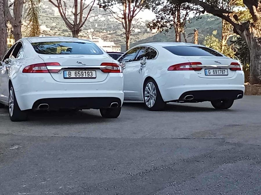 Rear view of two matching white Jaguar XF sedans
