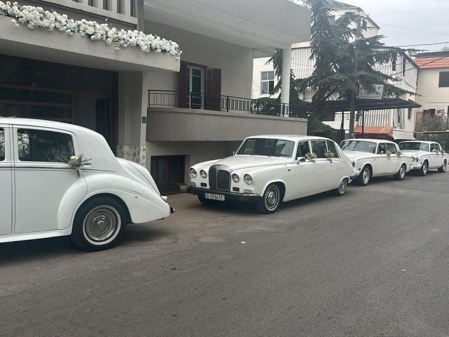 Row of white Daimler DS420 limousines outside a flower-decorated house