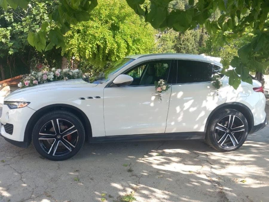 White Maserati Levante with a flower garland, side view under the trees