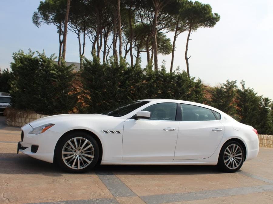 White Maserati Quattroporte, side view, in front of pine trees