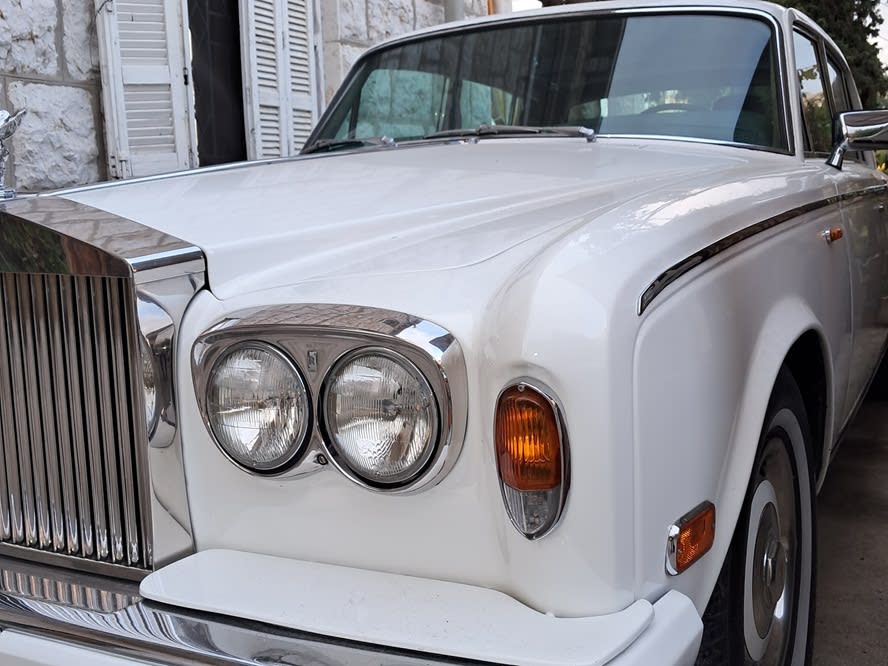 Close-up of the white Rolls-Royce Silver Shadow's round headlights and chrome grille