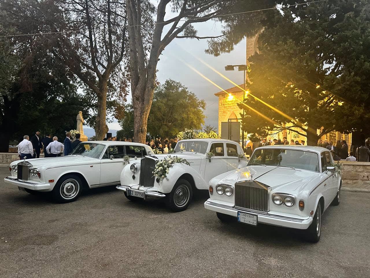 White 1953 Bentley R Type with flowers between two white Rolls-Royce Silver Shadows at sunset