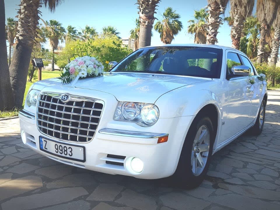 White Chrysler 300C with white flowers on the hood, palm trees behind