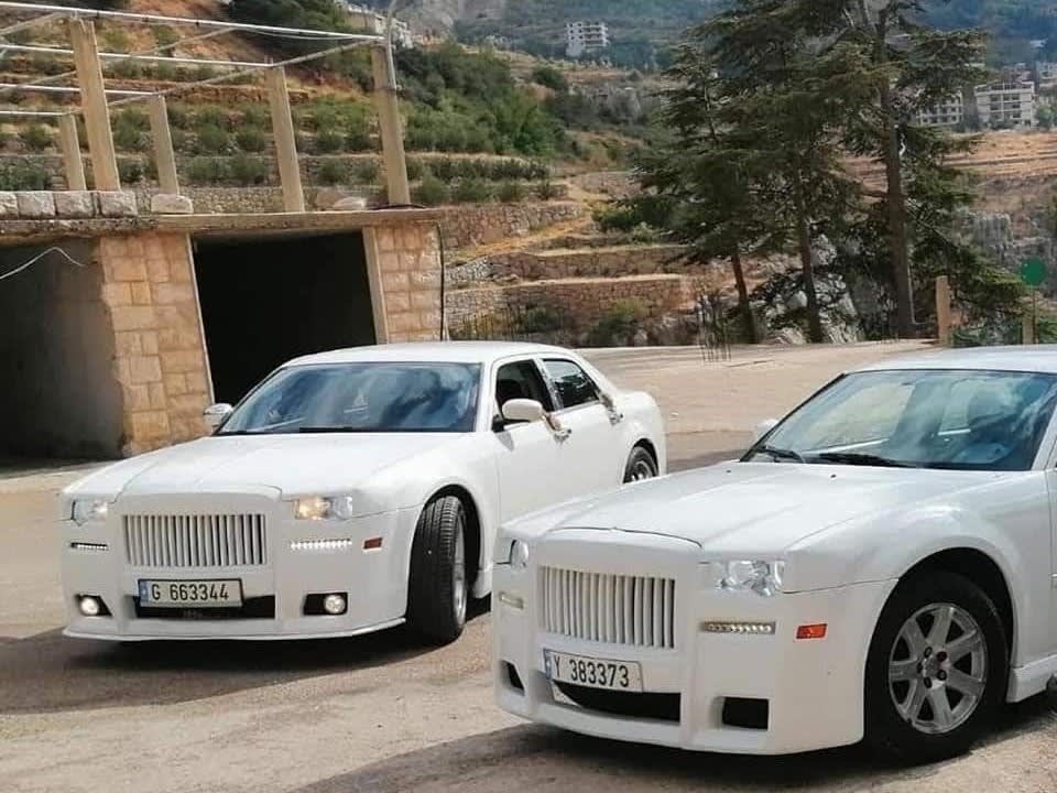 Two white Chrysler 300C Phantom-look sedans parked together by a stone arch
