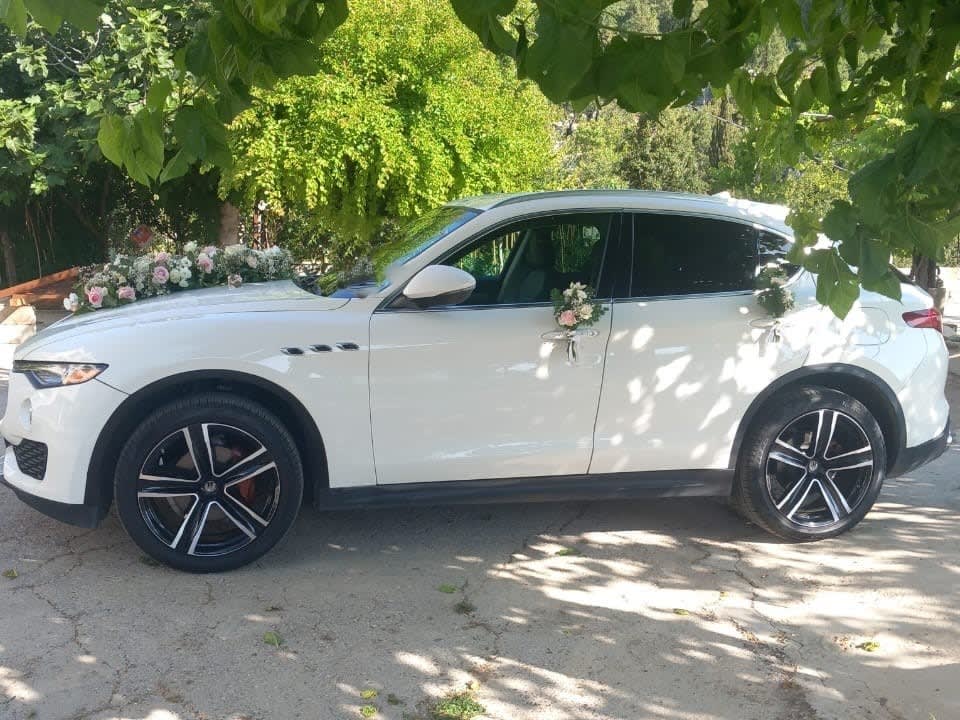 White Maserati Levante with a flower garland, side view under the trees
