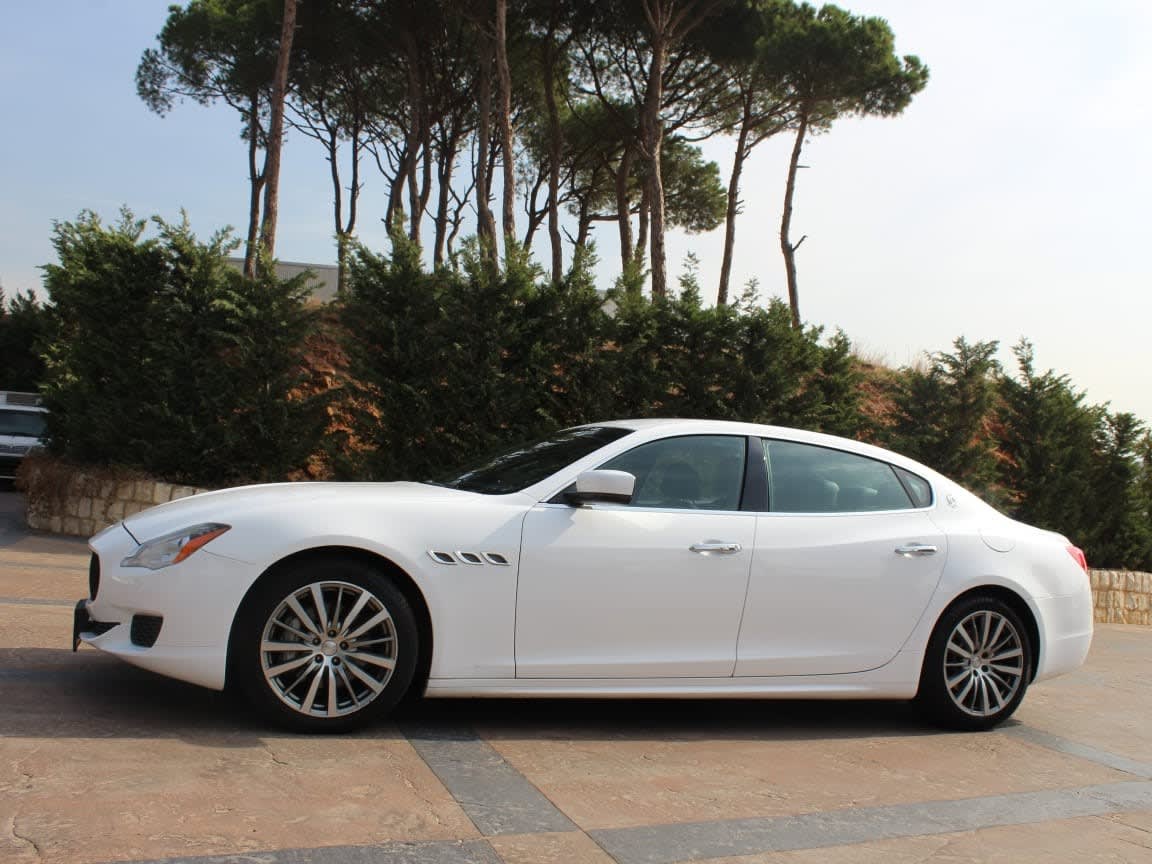 White Maserati Quattroporte, side view, in front of pine trees