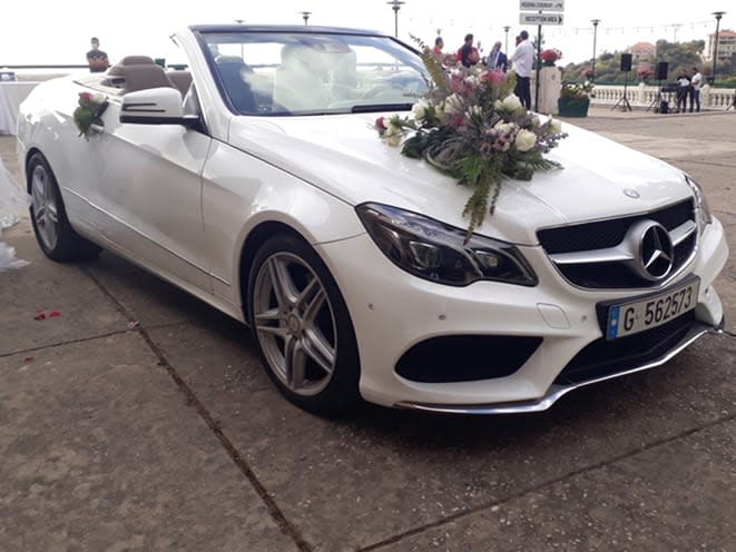 White Mercedes E-Class convertible, top down, with a flower bouquet on the hood in Adma