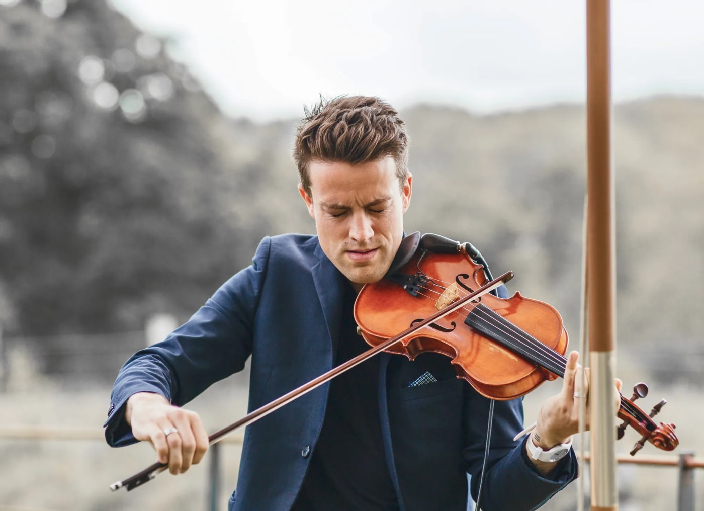Joel Grainger in a navy suit playing violin at a countryside Wedding
