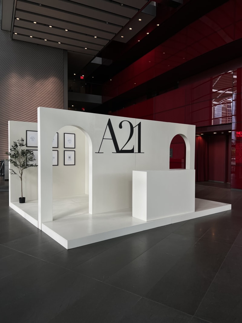 A modern, minimalist exhibition booth with a large "A21" logo and architectural elements in a dark, dramatic setting.
