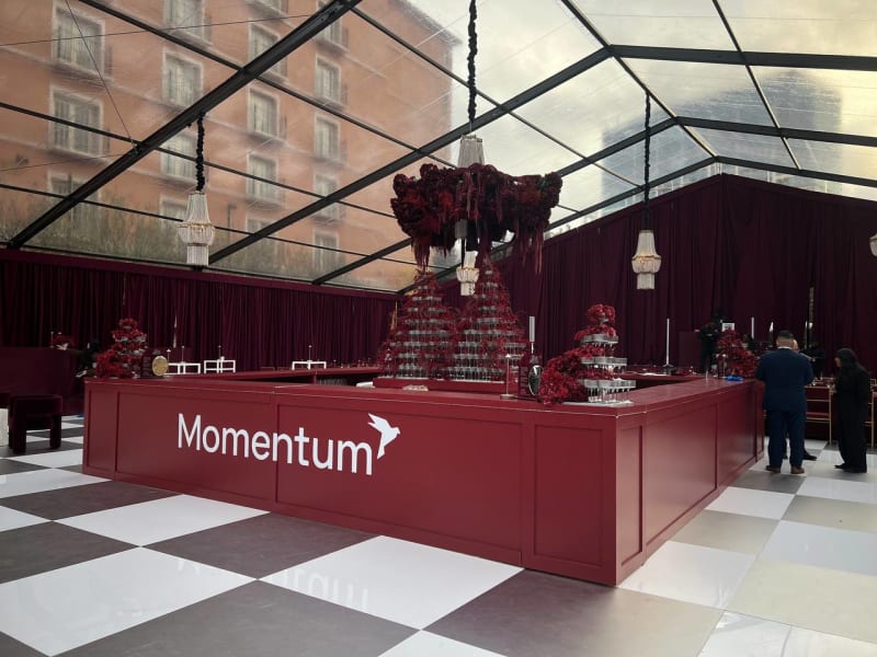 A large red counter with the word "Momentum" prominently displayed, surrounded by a lavish and ornate decor, including a chandelier and a checkered floor, in what appears to be an indoor event space or lobby.