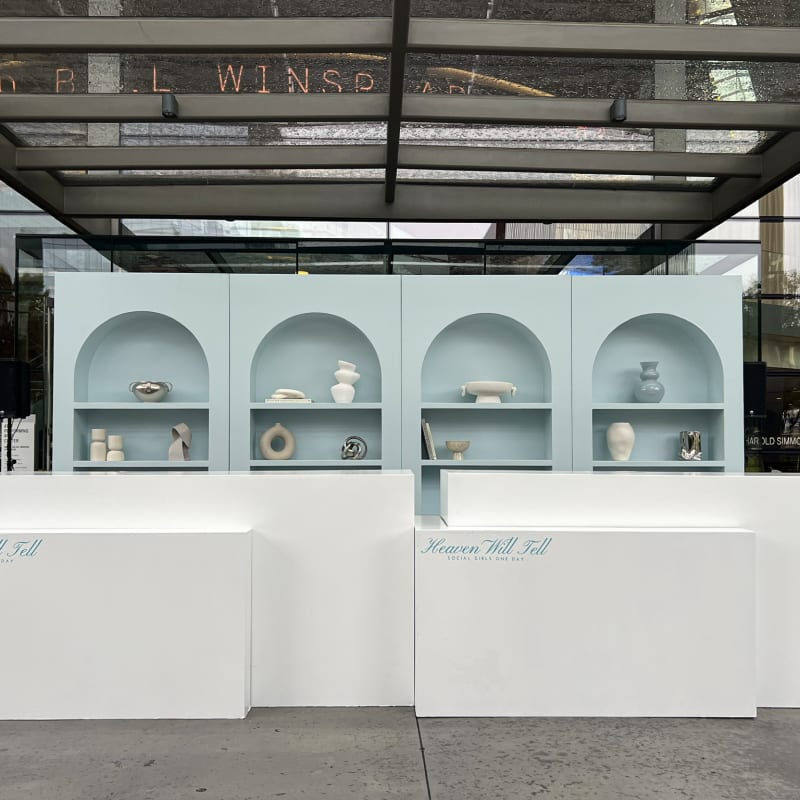 A modern, minimalist display featuring a series of arched shelves showcasing various ceramic and pottery items, set against a backdrop of an industrial-style building with the text "L WINS" visible.