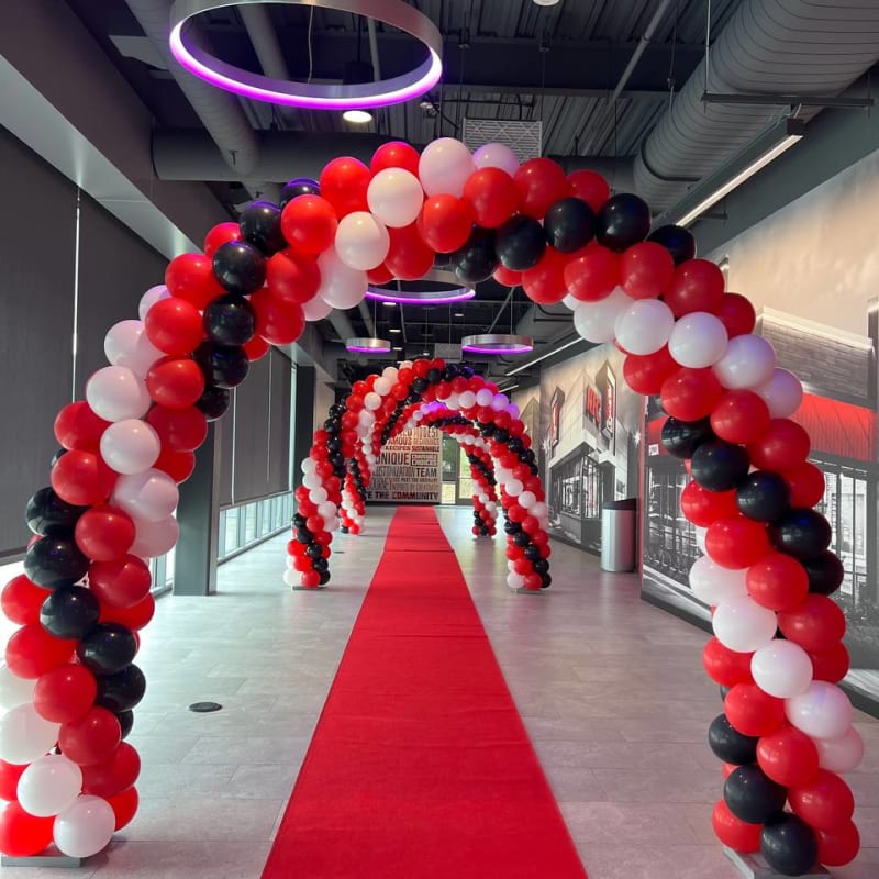 A large, red carpeted hallway is decorated with a large archway made of red ribbons and balloons, creating a festive atmosphere.