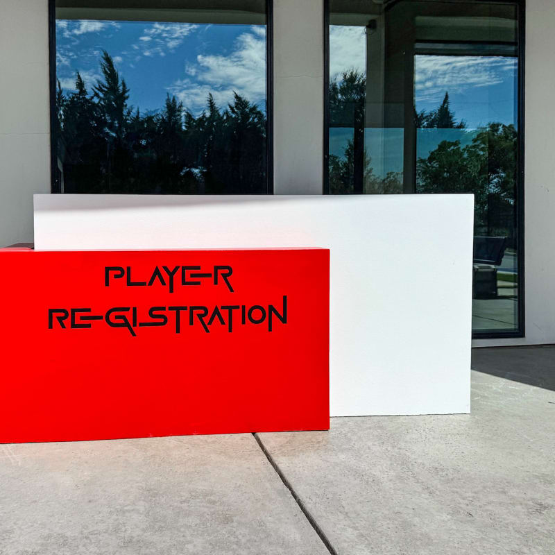 A large red sign reading "PLAYER RE-GISTRATION" stands in the foreground, with a glass building and trees visible in the background.