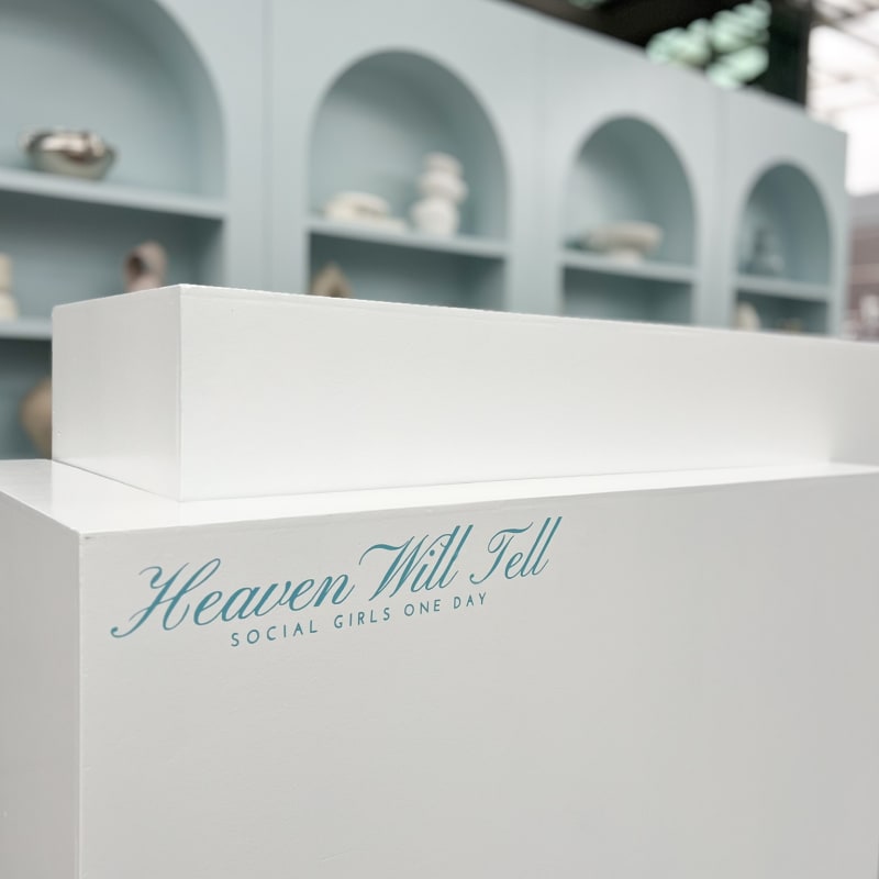 A white rectangular display box with the text "Heaven Will Tell" is placed in the foreground, against a backdrop of arched shelves.