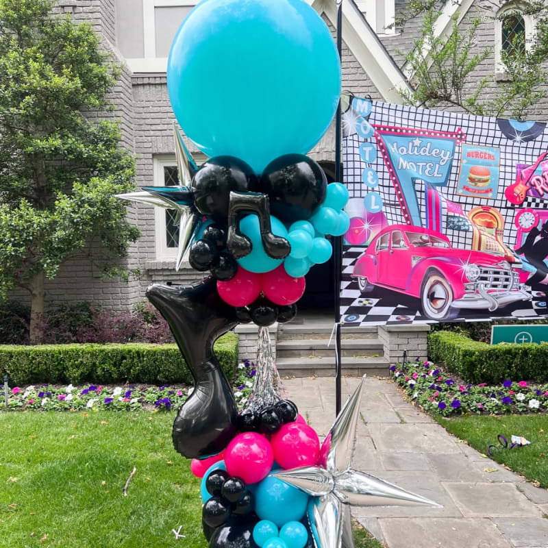 a bunch of balloons that are sitting on a pole in front of a house with a car in the background