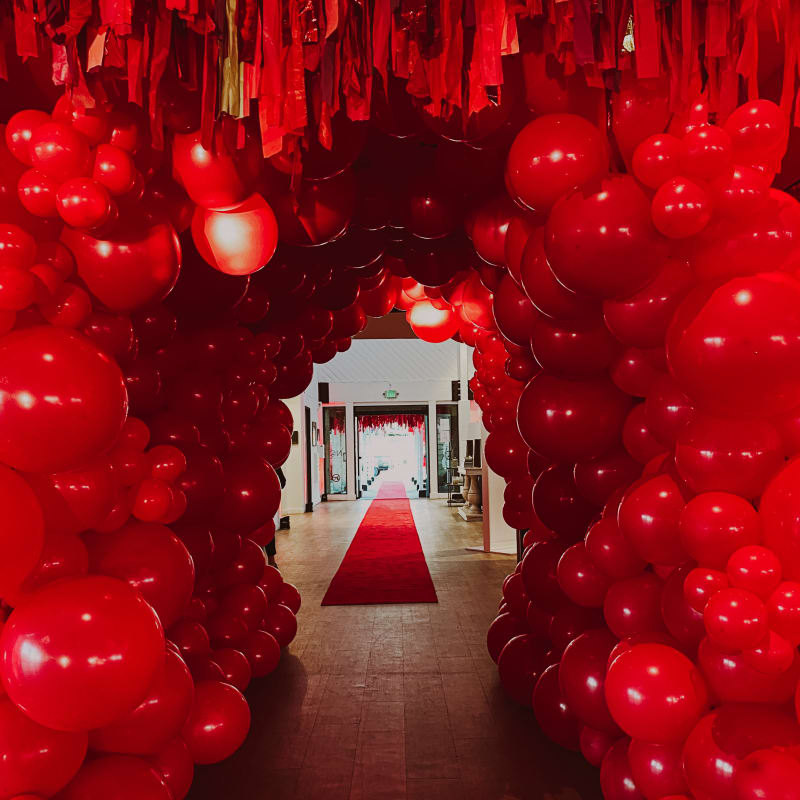 a hallway with red balloons hanging from the ceiling and a red carpet on the other side of the room