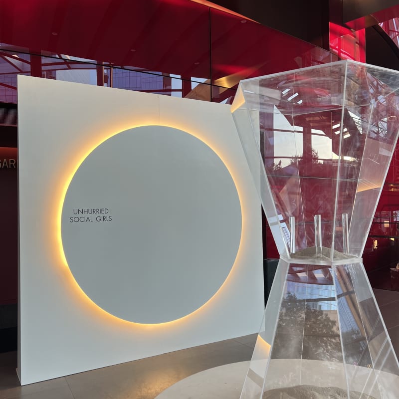 A large, illuminated circular display stands in the foreground, surrounded by a modern, minimalist interior with red and black accents in the background.