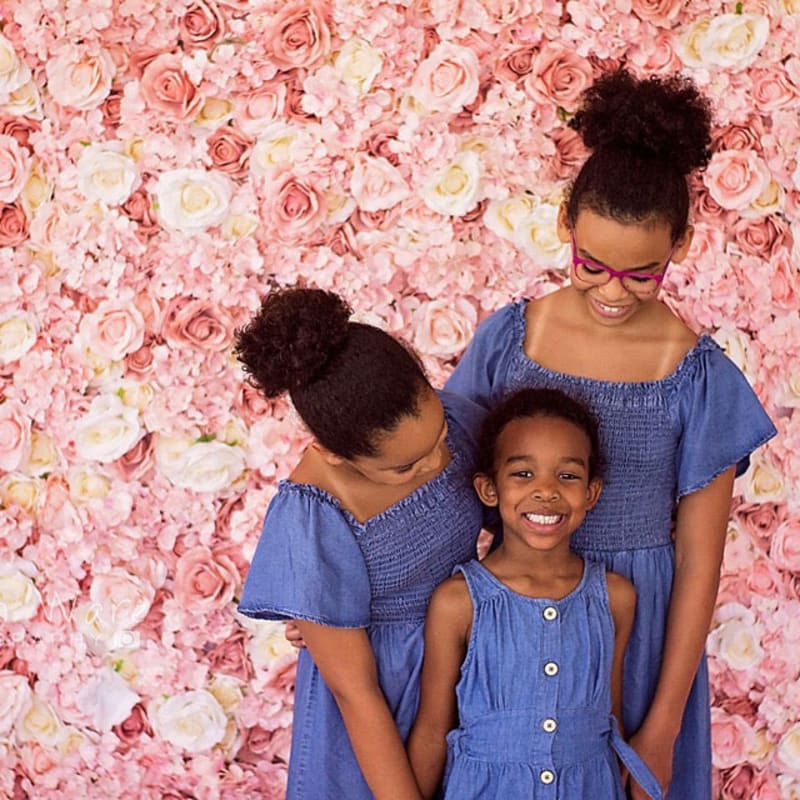 two young girls standing next to each other in front of a wall of pink and white flowers with their arms around each other