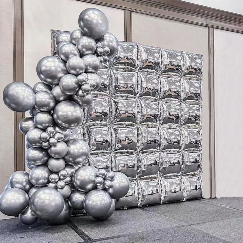 A large, abstract sculpture composed of shiny, metallic spheres of varying sizes is displayed against a backdrop of reflective glass panels.